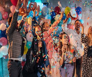 Group of young women and men having fun with balloons and photo booth at a party